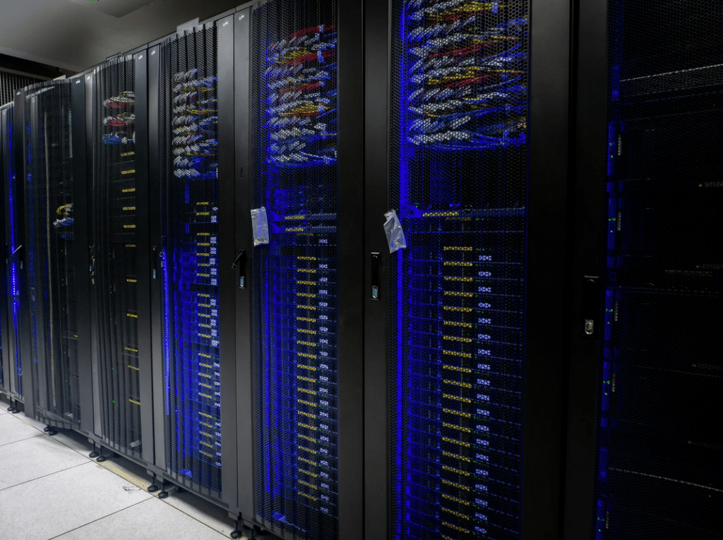 Rows of black server racks filled with computer hardware and illuminated blue lights in a data center.